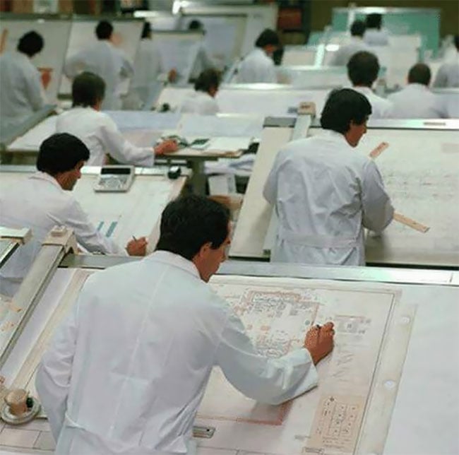 Delineantes con bata blanca sobre sus tableros; en primer plano,
                  un plano de instalaciones dibujado a tinta.