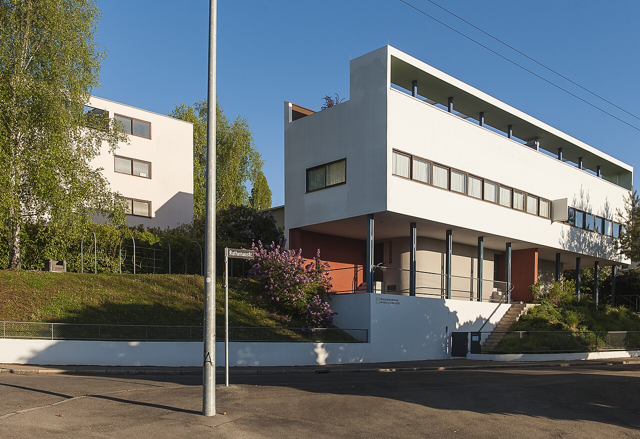 La casa doble de Le Corbusier en la Weissenhofsiedlung de
                    Stuttgart: un volumen blanco alargado sobre pilotis, con la
                    ventana corrida de lado a lado y la terraza arriba.