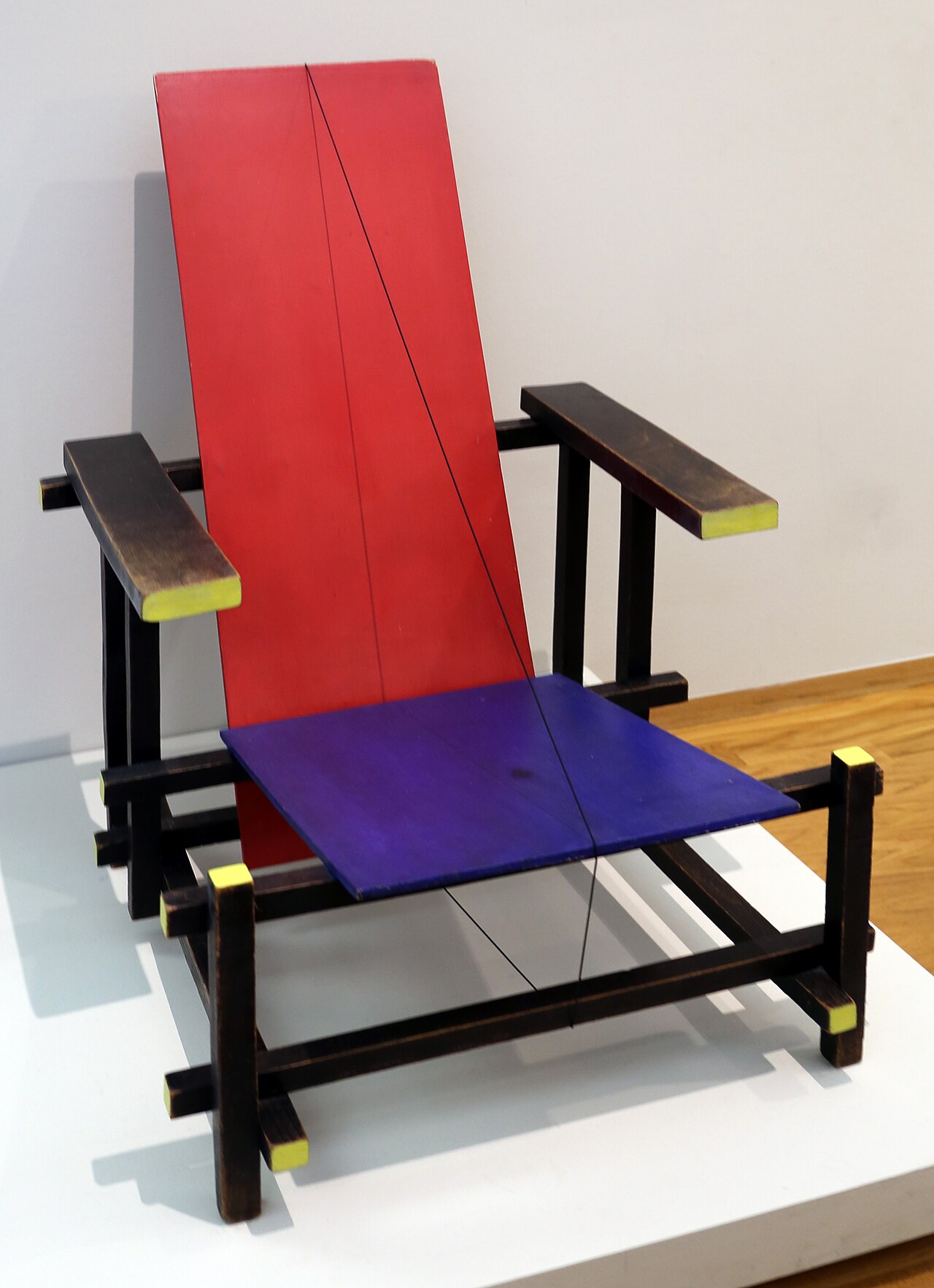 La silla roja y azul de Gerrit Rietveld: listones de madera
                    negros con los extremos amarillos, un respaldo rojo y un
                    asiento azul, todo en planos que se cruzan.